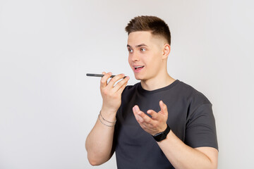 A young man, a guy talking to a friend on the phone, recording a voice message or a note in a smartphone application, holding a mobile phone near his lips close to the speaker, talking to an assistant