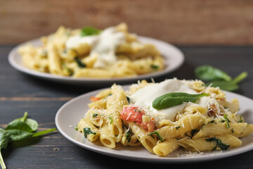 Two portions of pasta with tomatoes, spinach, parmesan and bolognese sauce. Dish in a plate on a wooden table.