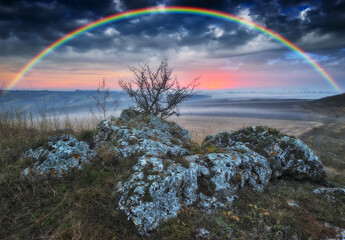 Rainbow with clouds over a rock