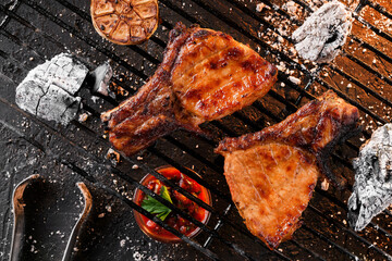 Grilled T-bone steak meat with garlic over the coals on a barbecue, dark background with light of fire. Top view