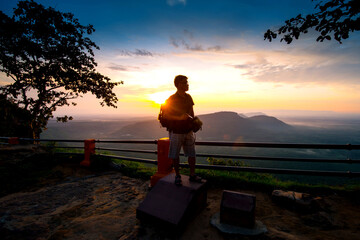 A photographer standing on top of Mountain at sunset with Mist.Asian male backpack in nature during sunset Relax time on holiday concept travel at Pha mor i dang,Sisaket province,Thailand,ASIA.