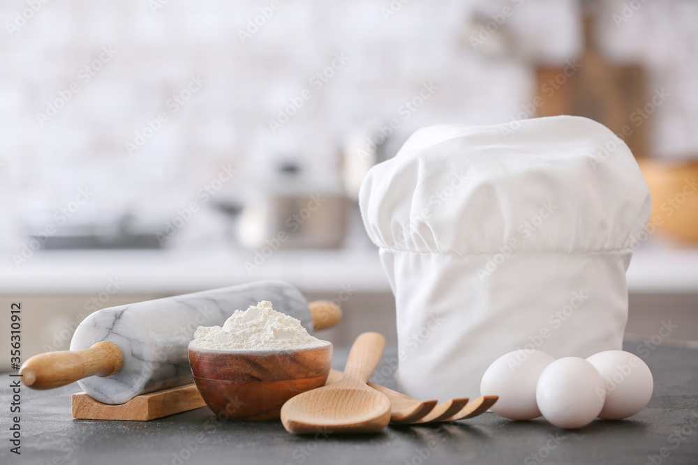 Chef's hat, utensils and products on table in kitchen