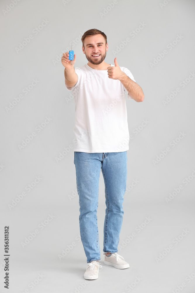 Young man with car key on grey background