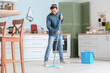 Handsome young man mopping floor in kitchen