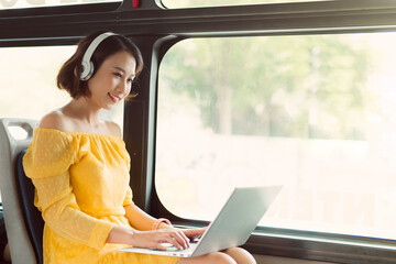 Wall Mural - Young businesswoman using laptop and listening to music when sitting on the bus.