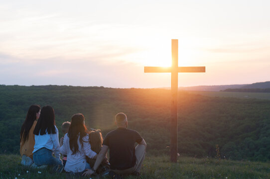 Christian family. Happy family on the nature. Children husband and wife. Wooden cross against the sky. Sunset. Cross. Crucifixion on the background of the sky. Easter. Calvary.