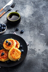 Wall Mural - Fritters of cottage cheese with blueberries. Cheese curd cheesecakes, pancakes on a dark concrete background. Copy space.