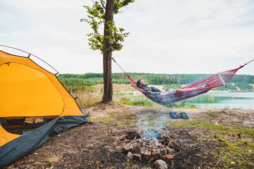 Wall Mural - man laying on hammock at lake beach near camp fire