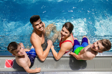 Top view of smiling family of four having fun and relaxing in indoor swimming pool at hotel resort.