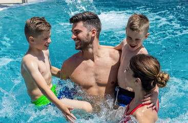 Wall Mural - smiling family of four having fun and relaxing in outdoor swimming pool at hotel resort.