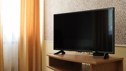 Hand holding a television remote control and surfing programs on television. watch, turn on or off the TV in the living room or bedroom on the black-screen nightstand. Copy space.