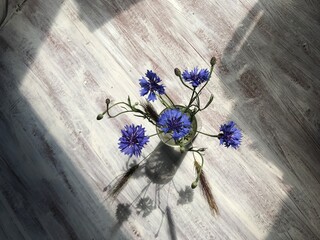 a small bouquet of flowers in a vase in a glass stands on the floor, the view from above, against the background of the white motley floor flat lay