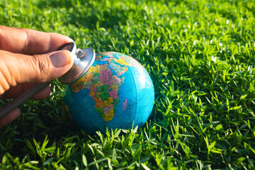 Hand and stethoscope with world on green grass.