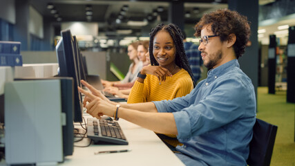 Wall Mural - University Library: Bright Black Girl and Smart Hispanic Boy Together Work on Computers, Chat, Discuss Class Assignment, Explain and Advice Each Other. Diverse Group of Students Exam Study Teamwork