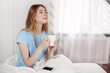 © Sviatlana - Beautiful girl drinking morning coffee sitting in bed. The girl is enjoying the morning, holding a Cup with a hot drink in her hands