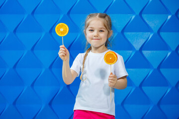 Beautiful young girl dressed in a white T-shirt holds half an orange in her hands and smiles. Orange fruits, she bites an orange and she likes.