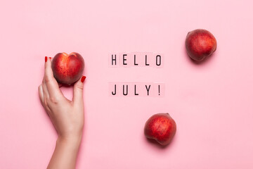 Wall Mural - Hello July text and female hand holds ripe peach on pink background. Hello July concept