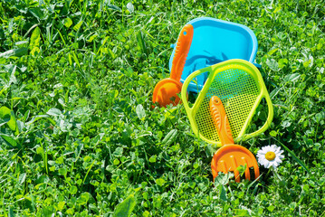 Wall Mural - Baby toys a shovel and bucket on green meadow background with copy space.