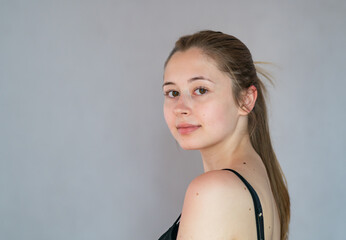 Wall Mural - Semi profile portrait of a languishing and charming young woman with ponytail hair posing looking at the camera on a grey background