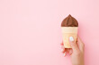 Young woman hand holding ice cream with chocolate glaze in waffle cup on pastel pink table background. Pastel color. Empty place for text. Closeup. Top down view.