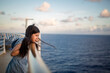 © Cavan Images - A young girl leans against a ship railing at sunset gazing at ocean
