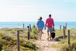 © Cavan Images - Back view of a young couple walking at beach with dog while holding hands