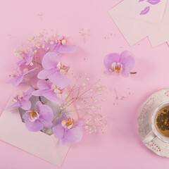 Wall Mural - Delicate flatlay composition with morning cup of tea, pink letter bag full of purple orchid flowers and empty envelop on light pink background