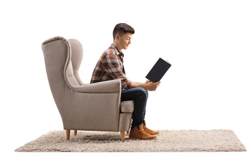 Profile shot of a young man sitting in an armchair and reading a book