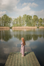 Redheaded Girl In Vintage Dress Standing Near Lake Seen From Back