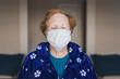 © Alvaro Sanchez/ADDICTIVE STOCK - Senior female with red hair in blue robe and medical mask looking at camera while standing in hospital room