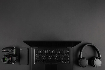  Creative dark flat lay with camera and laptop on black minimal table background with copy space