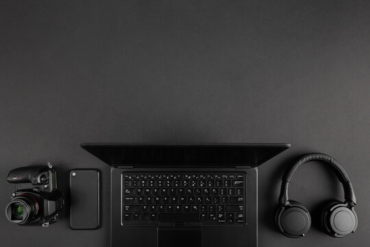  Creative dark flat lay with camera and laptop on black minimal table background with copy space