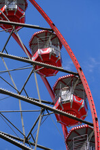 From Below Of Ferris Wheel With Red Cabins Located On Amusement Park On Sunny Day With Blue Sky