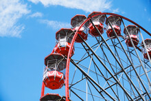 From Below Of Ferris Wheel With Red Cabins Located On Amusement Park On Sunny Day With Blue Sky
