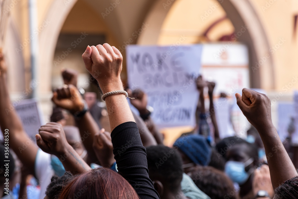 People raising fist with unfocused background in a pacifist protest against racism demanding justice - obrazy, fototapety, plakaty 