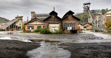 Wet Uneven Asphalt And Shabby Old One Story Deserted Wooden Houses On Background Of Green Trees And Abandoned Coal Mine On Cloudy Cool Day After Rain