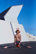 Handsome Athlete With Naked Torso Sitting On Iron Structure On Roof Of Building With Legs Spread Wide And Outstretched Toes And Looking At Camera