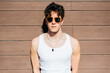 © Manuel Ruiz Alba/ADDICTIVE STOCK - Modern young handsome man in trendy sunglasses and white tank top standing near brown wall on sunny day on city street