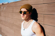 © Manuel Ruiz Alba/ADDICTIVE STOCK - Modern young handsome man in trendy sunglasses and beanie hat and white tank top standing near brown wall on sunny day on city street