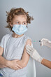 © PHILIPPE DEGROOTE/ADDICTIVE STOCK - Crop nurse in white latex gloves holding shoulder of boy with curly hair while giving vaccine injection with syringe in modern clinic