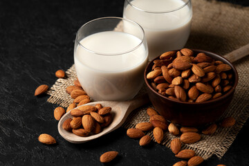 almond milk without sugar and lactose in glass with sprinkled nuts, vegetarian milk drink on a dark black table