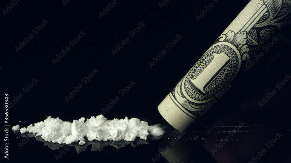 Line of cocaine being snorted up rolled up dollar bill on black reflective  table top. Stock Photo