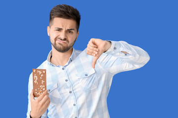 Sticker - Displeased young man with tasty chocolate showing thumb-down on color background