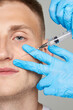 Injection Male face treatment. Close-up of a man receiving anti-aging skin care. Cosmetology procedures in the clinic. Beautician hands in gloves with a syringe.
