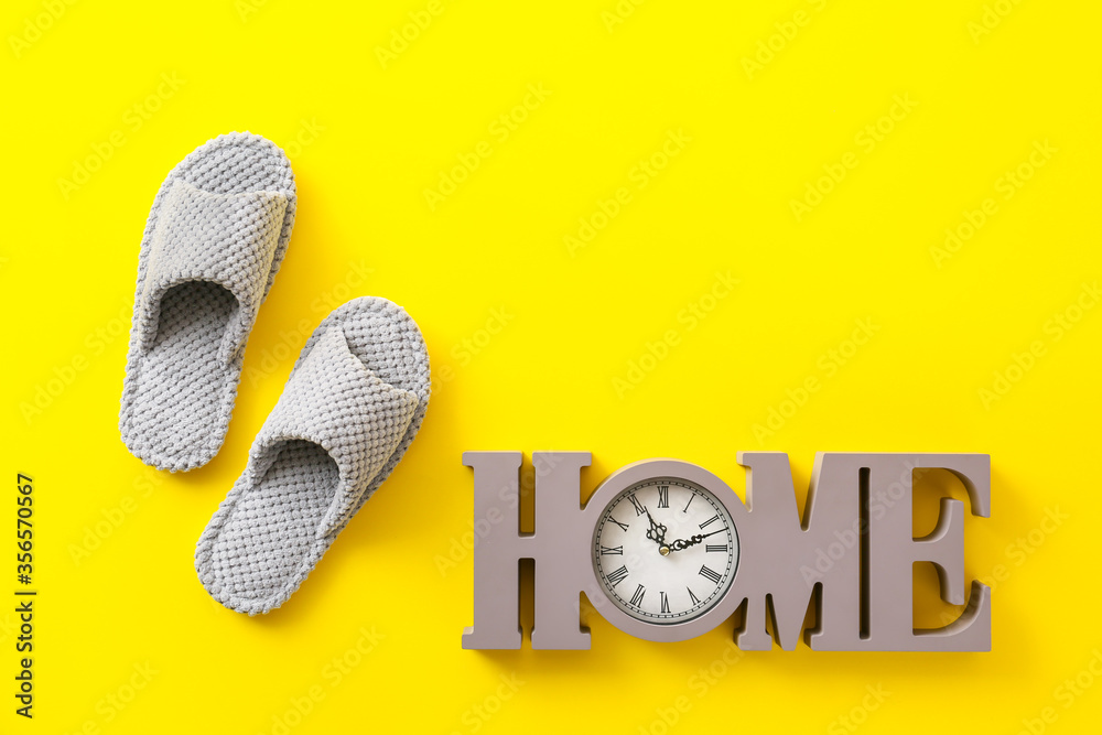 Pair of soft slippers and decorative clock on color background