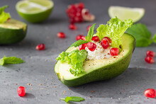 Halved Avocado With Cream Cheese, Pomegranate Seeds, Lettuce, Mint And Lime On Grey Stone Background. Healthy Food Concept. Close Up.