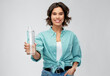 © Syda Productions - people concept - portrait of happy smiling young woman in turquoise shirt holding water in reusable glass bottle grey background