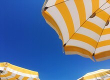 Low Angle Bottom View And Detail Of Yellow And White Beach Or Poolside Umbrellas With A Blue Sky In The Background - Holiday And Vacation Concept