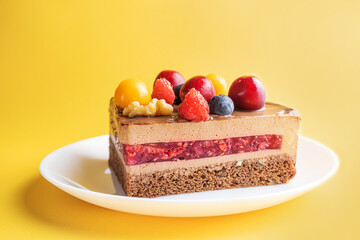 A piece of chocolate berry cake in a white plate on a yellow background. The concept of homemade food, sweets. Minimalism.