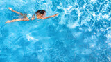 Fototapeta  - Active young girl in swimming pool aerial top view from above, child relaxes and swims on inflatable ring donut and has fun in water on family vacation, tropical holiday resort
